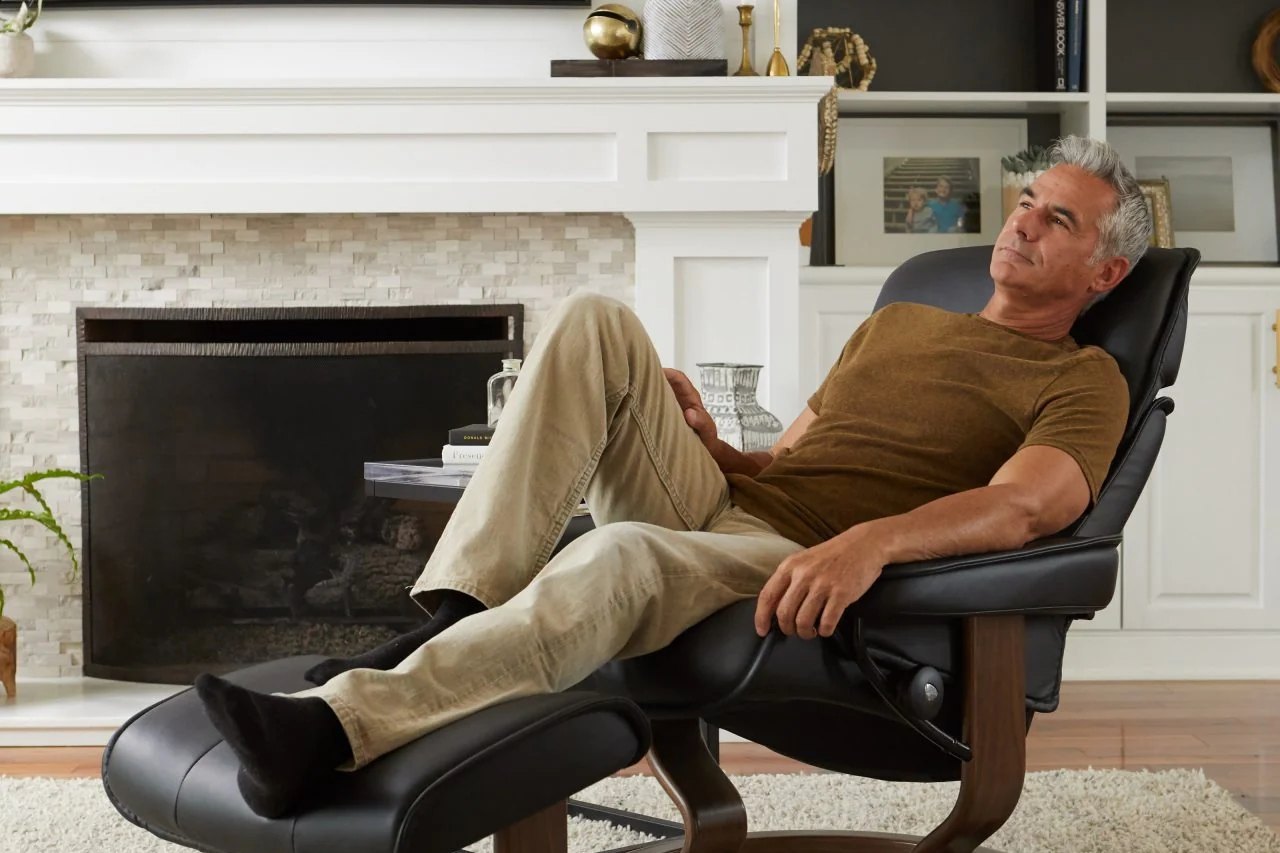 Man relaxing in a Stressless Admiral recliner with ottoman in front of a fireplace