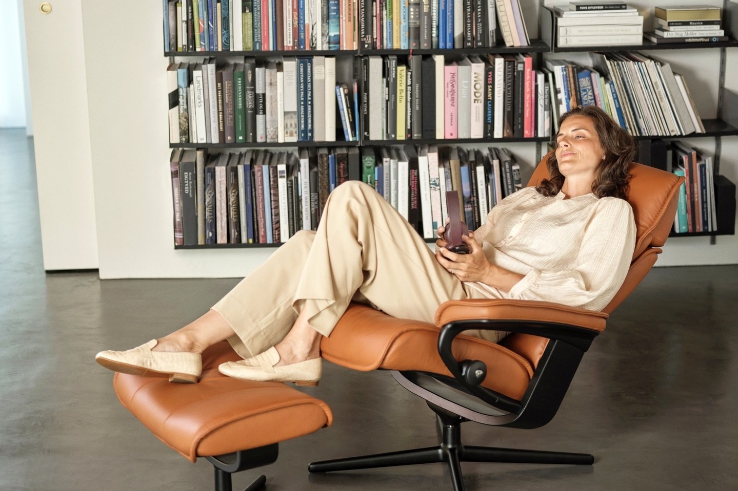 Woman reading in a Stressless Admiral Cross base recliner in Paloma New Cognac leather