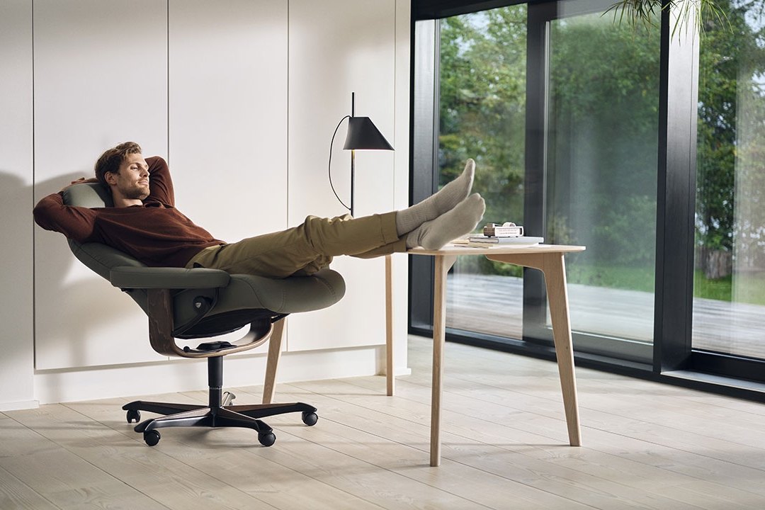 Man reclining in a Stressless Consul office chair beside a desk by the window